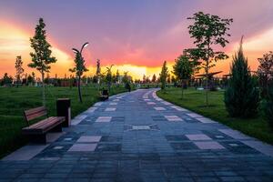 città parco nel presto estate o primavera con marciapiede, lanterne, giovane verde prato, alberi e drammatico nuvoloso cielo su un' tramonto o Alba. foto