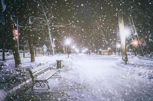 nevicata nel un' inverno parco a notte con raggiante lanterne, marciapiede coperto con neve e alberi. Vintage ▾ film estetico. foto