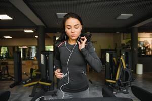 giovane in forma donna in esecuzione su routine ascoltando per musica attraverso cuffie a palestra. concetto di salutare stile di vita foto