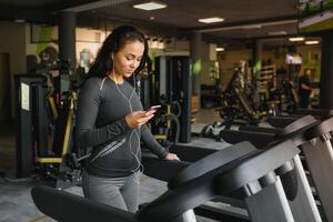 giovane in forma donna in esecuzione su routine ascoltando per musica attraverso cuffie a palestra. concetto di salutare stile di vita foto