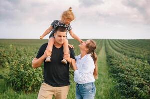 contento famiglia con poco figlia la spesa tempo insieme nel soleggiato campo. foto