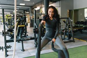 bella ispanico giovane donna fare alcuni CrossFit esercizi con un' corda a un' palestra. foto