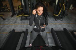 giovane in forma donna in esecuzione su routine ascoltando per musica attraverso cuffie a palestra. concetto di salutare stile di vita foto