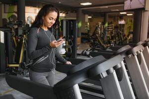 giovane in forma donna in esecuzione su routine ascoltando per musica attraverso cuffie a palestra. concetto di salutare stile di vita foto