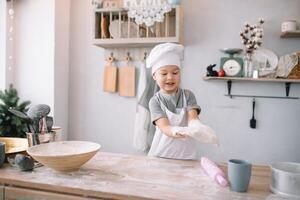 giovane ragazzo carino su il cucina cucinare capocuoco nel bianca uniforme e cappello vicino tavolo. fatti in casa Pan di zenzero. il ragazzo cucinato il cioccolato biscotti. foto