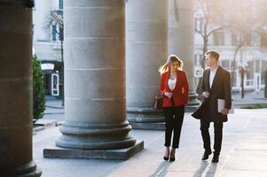 attività commerciale donna e attività commerciale uomo uso smartphone e parlare su il occupato grande città strada. tutti e due Guarda squisitamente elegante. foto