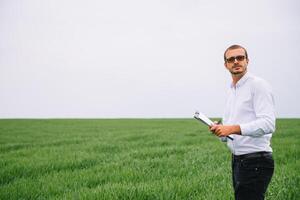 giovane agronomo detiene tavoletta toccare tampone computer nel verde Grano campo. agribusiness concetto. agricolo ingegnere in piedi nel un' Grano campo con un' tavoletta nel estate foto