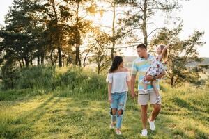 contento famiglia a piedi nel il parco. mamma, papà e figlia camminare all'aperto, genitori Tenere il bambino ragazze mani. infanzia, genitorialità, famiglia obbligazioni, matrimonio concetto. foto