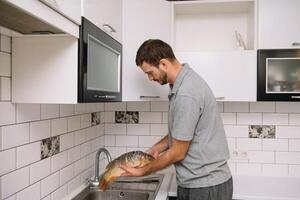 uomo taglio fresco pesce nel cucina nel casa. uomo macellazione pesce per cucinare. foto