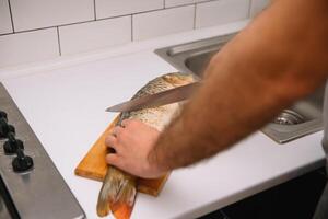 uomo taglio fresco pesce nel cucina nel casa. uomo macellazione pesce per cucinare. foto