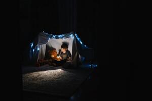 bambino ragazzo lettura con libro e torcia elettrica e orsacchiotto orso nel tenda. prima andando per letto. foto