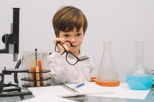 il ragazzo con un' microscopio e vario colorato fiaschi su un' bianca sfondo. un' ragazzo fare esperimenti nel il laboratorio. esplosione nel il laboratorio. scienza e formazione scolastica foto