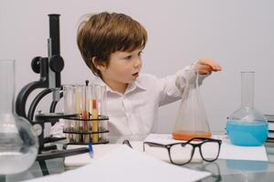 il ragazzo con un' microscopio e vario colorato fiaschi su un' bianca sfondo. un' ragazzo fare esperimenti nel il laboratorio. esplosione nel il laboratorio. scienza e formazione scolastica foto