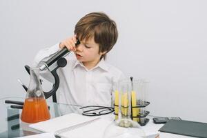 il ragazzo con un' microscopio e vario colorato fiaschi su un' bianca sfondo. un' ragazzo fare esperimenti nel il laboratorio. esplosione nel il laboratorio. scienza e formazione scolastica. foto