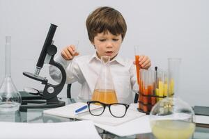 il ragazzo con un' microscopio e vario colorato fiaschi su un' bianca sfondo. un' ragazzo fare esperimenti nel il laboratorio. esplosione nel il laboratorio. scienza e formazione scolastica foto