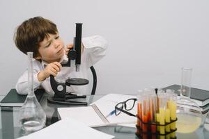 il ragazzo con un' microscopio e vario colorato fiaschi su un' bianca sfondo. un' ragazzo fare esperimenti nel il laboratorio. esplosione nel il laboratorio. scienza e formazione scolastica foto