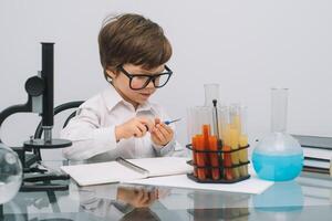 il ragazzo con un' microscopio e vario colorato fiaschi su un' bianca sfondo. un' ragazzo fare esperimenti nel il laboratorio. esplosione nel il laboratorio. scienza e formazione scolastica foto