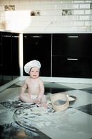 poco ragazzo seduta su tappeto nel cucina giocando con cucinando pentole. carino ragazzo cucinando nel cucina a casa foto