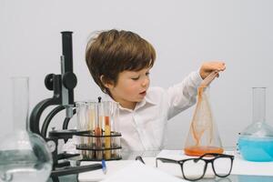 il ragazzo con un' microscopio e vario colorato fiaschi su un' bianca sfondo. un' ragazzo fare esperimenti nel il laboratorio. esplosione nel il laboratorio. scienza e formazione scolastica foto