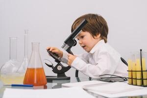 il ragazzo con un' microscopio e vario colorato fiaschi su un' bianca sfondo. un' ragazzo fare esperimenti nel il laboratorio. esplosione nel il laboratorio. scienza e formazione scolastica. foto