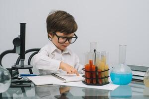 il ragazzo con un' microscopio e vario colorato fiaschi su un' bianca sfondo. un' ragazzo fare esperimenti nel il laboratorio. esplosione nel il laboratorio. scienza e formazione scolastica foto