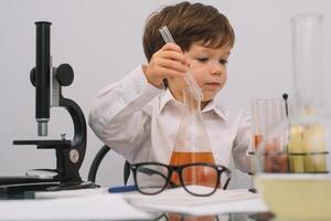 il ragazzo con un' microscopio e vario colorato fiaschi su un' bianca sfondo. un' ragazzo fare esperimenti nel il laboratorio. esplosione nel il laboratorio. scienza e formazione scolastica foto