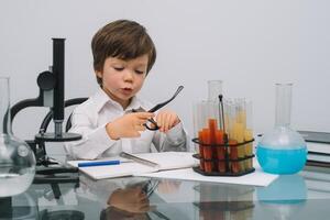 il ragazzo con un' microscopio e vario colorato fiaschi su un' bianca sfondo. un' ragazzo fare esperimenti nel il laboratorio. esplosione nel il laboratorio. scienza e formazione scolastica foto