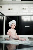 poco ragazzo seduta su tappeto nel cucina giocando con cucinando pentole. carino ragazzo cucinando nel cucina a casa foto