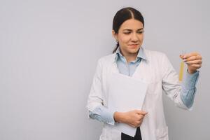 femmina medico nel bianca uniforme è Tenere fiaschi mentre in piedi contro bianca sfondo foto