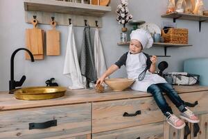 giovane contento mamma e sua bambino cucinare biscotti a casa nel il cucina. Natale fatti in casa Pan di zenzero. carino ragazzo con madre nel bianca uniforme e cappello cucinato cioccolato biscotti. foto