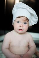 poco ragazzo seduta su tappeto nel cucina giocando con cucinando pentole. carino ragazzo cucinando nel cucina a casa foto