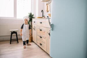 giovane ragazzo carino su il cucina cucinare capocuoco nel bianca uniforme e cappello vicino tavolo. Natale fatti in casa Pan di zenzero. il ragazzo cucinato il cioccolato biscotti. foto