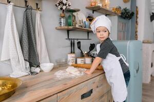 giovane ragazzo carino su il cucina cucinare capocuoco nel bianca uniforme e cappello vicino tavolo. Natale fatti in casa Pan di zenzero. il ragazzo cucinato il cioccolato biscotti. foto