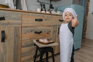 giovane contento mamma e sua bambino cucinare biscotti a casa nel il cucina. Natale fatti in casa Pan di zenzero. carino ragazzo con madre nel bianca uniforme e cappello cucinato cioccolato biscotti foto