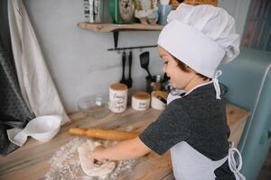 giovane ragazzo carino su il cucina cucinare capocuoco nel bianca uniforme e cappello vicino tavolo. Natale fatti in casa Pan di zenzero. il ragazzo cucinato il cioccolato biscotti. foto