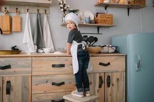 giovane contento mamma e sua bambino cucinare biscotti a casa nel il cucina. Natale fatti in casa Pan di zenzero. carino ragazzo con madre nel bianca uniforme e cappello cucinato cioccolato biscotti. foto