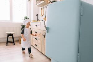 giovane contento mamma e sua bambino cucinare biscotti a casa nel il cucina. Natale fatti in casa Pan di zenzero. carino ragazzo con madre nel bianca uniforme e cappello cucinato cioccolato biscotti. foto