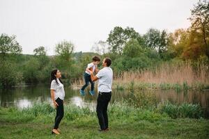 contento famiglia madre padre e bambino figlio su natura su tramonto. mamma, papà e ragazzo ridendo e abbracciare, godendo natura fuori. soleggiato giorno, bene umore. concetto di un' contento famiglia. foto