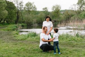 contento famiglia madre padre e bambino figlio su natura su tramonto. mamma, papà e ragazzo ridendo e abbracciare, godendo natura fuori. soleggiato giorno, bene umore. concetto di un' contento famiglia. foto