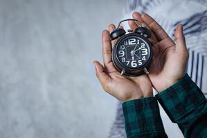 tempo gestione concetto. uomo mani Tenere nero retrò allarme orologio. tempo per scia su per il mattina routine foto