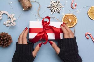 capodanno disteso con un regalo in mano. una ragazza con un maglione tiene una scatola con un fiocco in mano sullo sfondo di decorazioni natalizie