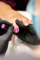 pittura Chiodi di un' donna. mani di manicure nel nero guanti l'applicazione rosa chiodo polacco su femmina Chiodi nel un' bellezza salone. foto