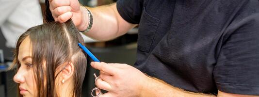 parrucchiere divide femmina capelli in sezioni con pettine Tenere capelli con sua mani nel capelli salone vicino su. foto