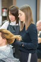 Due femmina parrucchieri preparare lungo capelli di un' giovane donna fabbricazione riccioli acconciatura nel un' bellezza salone. foto