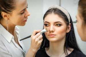 avvicinamento ritratto di un' donna l'applicazione asciutto cosmetico tonale fondazione su il viso utilizzando un' trucco spazzola. trucco dettaglio. foto