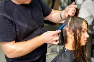 parrucchiere divide femmina capelli in sezioni con pettine Tenere capelli con sua mani nel capelli salone vicino su. foto