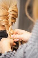 intrecciare treccia. mani di femmina parrucchiere trecce lungo treccia per un' bionda donna nel un' capelli salone. foto