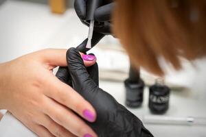 pittura Chiodi di un' donna. mani di manicure nel nero guanti l'applicazione rosa chiodo polacco su femmina Chiodi nel un' bellezza salone. foto