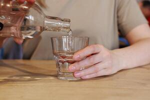 mano scrosciante acqua a partire dal bottiglia in bicchiere a di legno tavolo foto