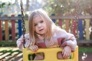 adorabile bambino piccolo ragazza giocando su un' swing impostato nel un' colorato terreno di gioco. foto